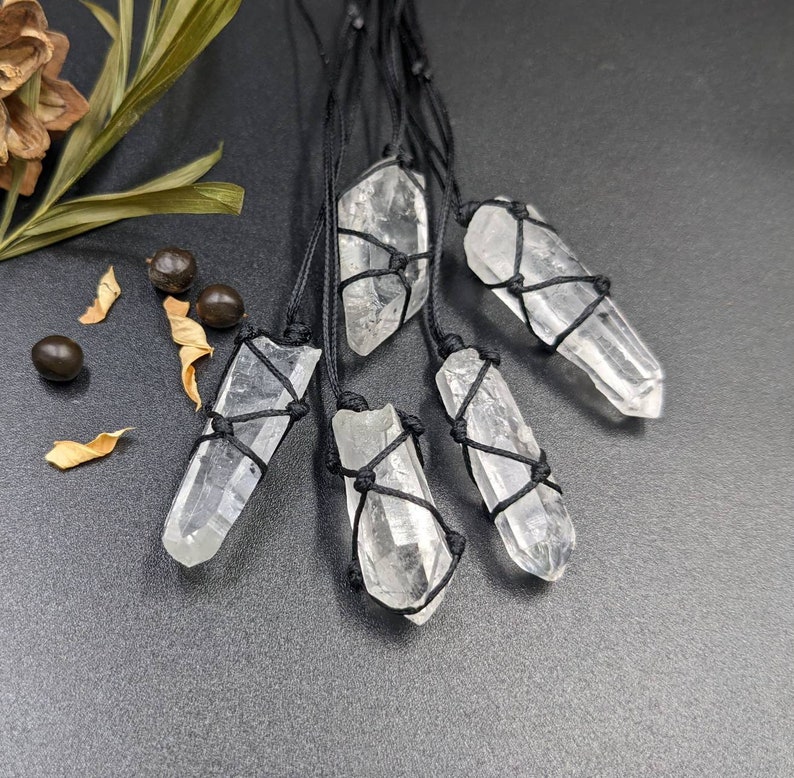 May include: Five clear quartz crystal pendants with black string tied around them. The crystals are all different shapes and sizes.