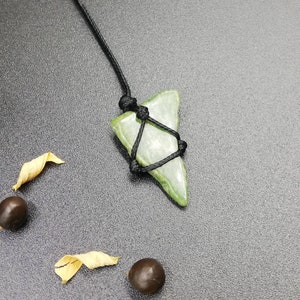 Pu&ograve; includere: Un ciondolo in pietra verde a forma di pinna di squalo, legato con un cordoncino nero.