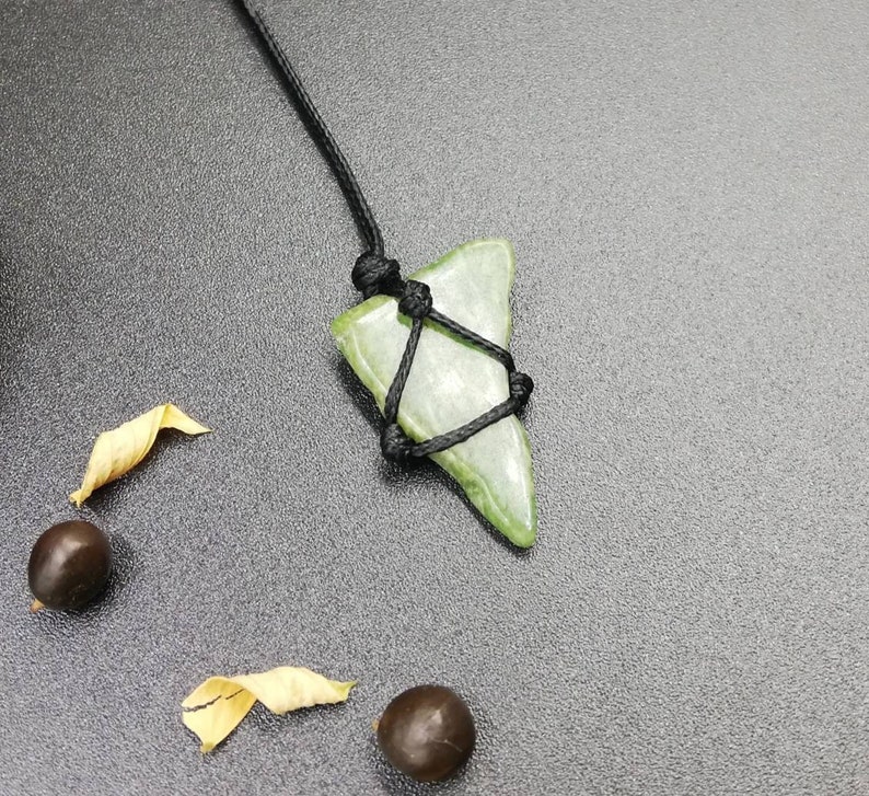 Pu&ograve; includere: Un ciondolo in pietra verde a forma di pinna di squalo, legato con un cordoncino nero.