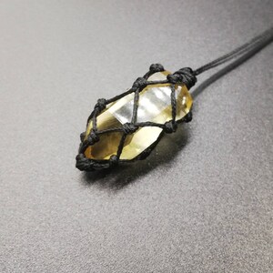 May include: A yellow crystal encased in a black macrame net, hanging from a black cord.