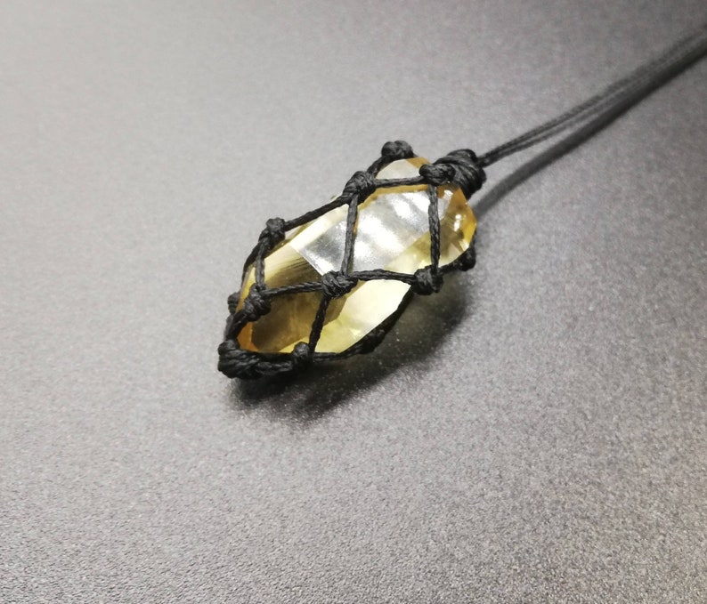 May include: A yellow crystal encased in a black macrame net, hanging from a black cord.