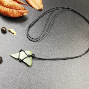 Pu&ograve; includere: Un ciondolo di pietra verde a forma di triangolo, legato a una collana di cordoncino nero.