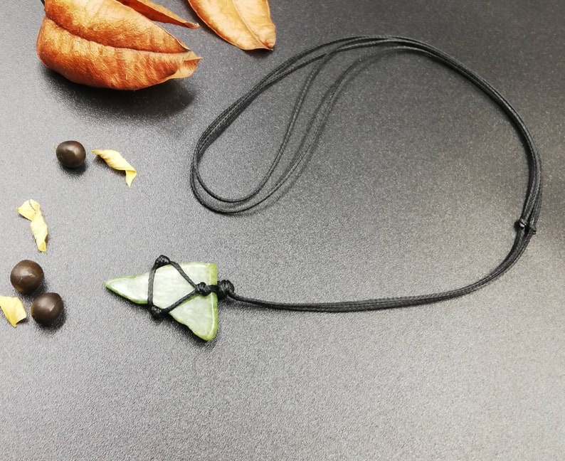 Pu&ograve; includere: Un ciondolo di pietra verde a forma di triangolo, legato a una collana di cordoncino nero.