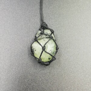 May include: A green gemstone pendant in a black macrame knot necklace.