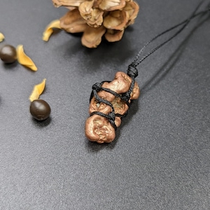 May include: A copper nugget pendant necklace with a black cord. The nugget is irregularly shaped and has a rough, textured surface. The cord is tied in a knot around the nugget.