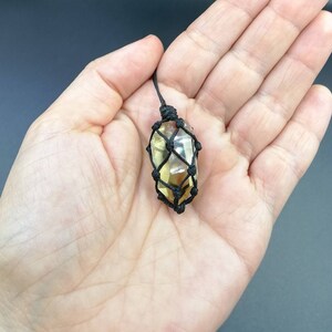 May include: A yellow crystal pendant in a black macrame knot. The crystal is faceted and has a natural, raw look. The pendant is hanging from a black cord.