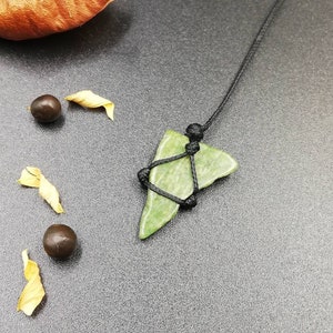 Pu&ograve; includere: Un ciondolo in pietra verde con una collana in corda nera. La pietra ha la forma di un triangolo e una texture ruvida. Il cordino &egrave; annodato nella parte superiore del ciondolo.
