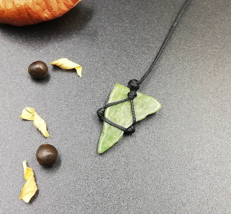 Pu&ograve; includere: Un ciondolo in pietra verde con una collana in corda nera. La pietra ha la forma di un triangolo e una texture ruvida. Il cordino &egrave; annodato nella parte superiore del ciondolo.