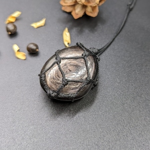 May include: A black obsidian stone pendant with a black cord wrapped around it in a geometric pattern.