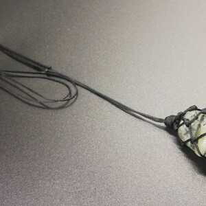 May include: A green stone pendant with black string knotted around it, hanging from a black cord.