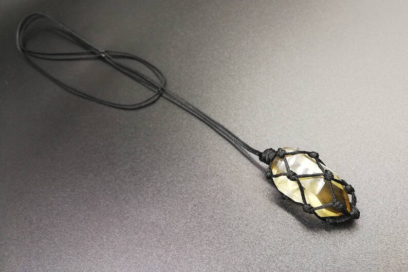 May include: A yellow crystal pendant encased in a black macrame knot necklace.
