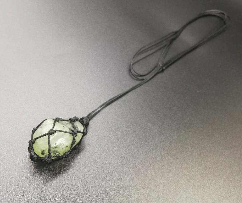 May include: A green crystal stone wrapped in black cord, hanging from a black cord necklace.