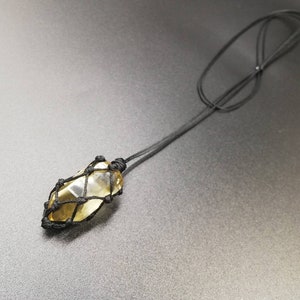 May include: A yellow citrine crystal wrapped in a black macrame cord, hanging from a black cord necklace.
