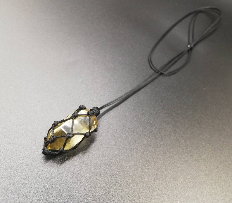 May include: A yellow citrine crystal wrapped in a black macrame cord, hanging from a black cord necklace.