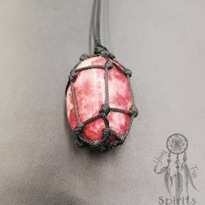 May include: A pink and white gemstone pendant with a black macrame knotting, hanging from a black cord.