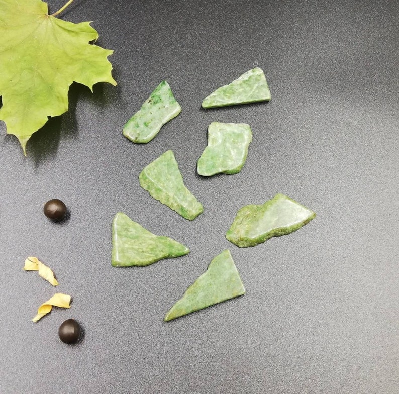 Pu&ograve; includere: Sette pezzi di pietra di giada verde di diverse forme e dimensioni. Le pietre sono disposte su una superficie grigia.