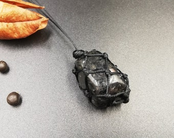 May include: A black gemstone pendant with a black cord necklace. The gemstone is wrapped in a black net-like material.
