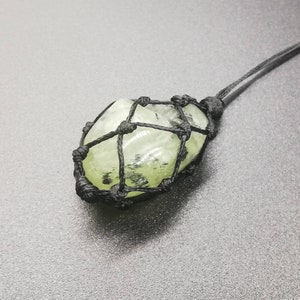 May include: A green crystal stone wrapped in a black macrame knot pendant.