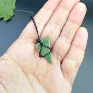 Pu&ograve; includere: Un ciondolo di pietra verde su una collana di cordoncino nero. La pietra ha una forma triangolare e una texture ruvida e naturale.