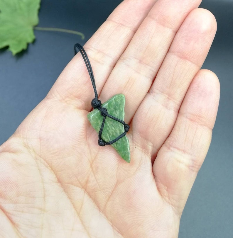 Pu&ograve; includere: Un ciondolo di pietra verde su una collana di cordoncino nero. La pietra ha una forma triangolare e una texture ruvida e naturale.