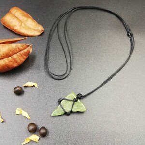 Pu&ograve; includere: Un ciondolo di pietra verde a forma di triangolo appeso a una collana di cordoncino nero. Il ciondolo &egrave; legato al cordoncino con uno spago nero.