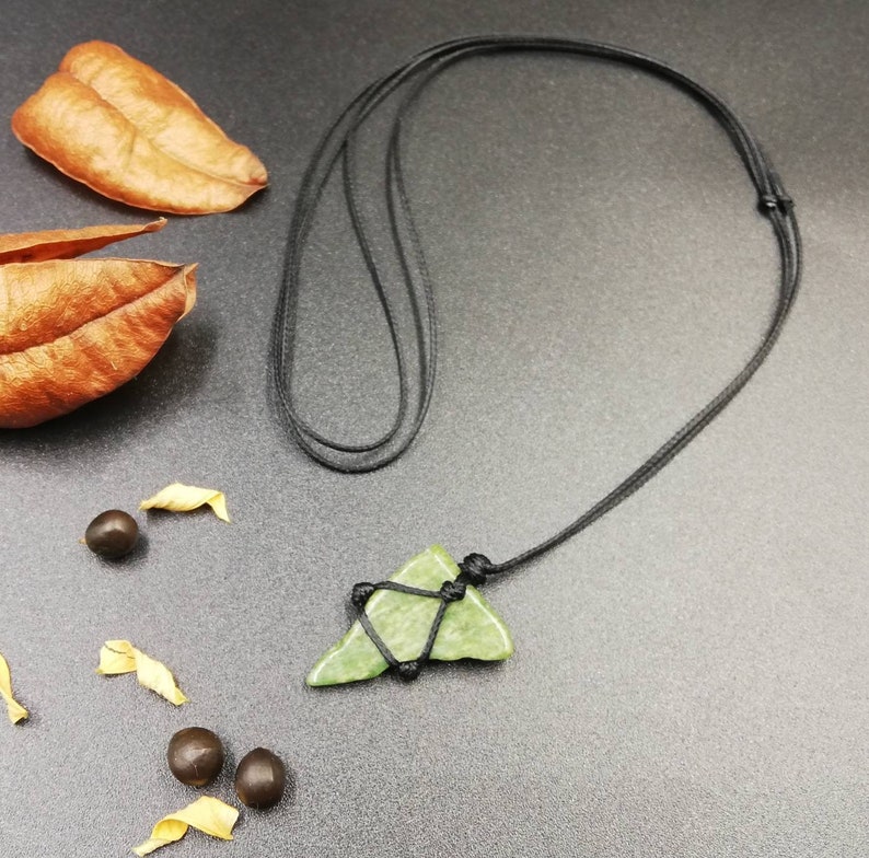 Pu&ograve; includere: Un ciondolo di pietra verde a forma di triangolo appeso a una collana di cordoncino nero. Il ciondolo &egrave; legato al cordoncino con uno spago nero.