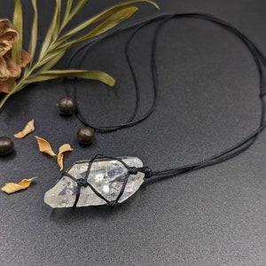 May include: A clear quartz crystal pendant on a black cord necklace. The crystal is wrapped with black cord and has a raw, natural shape.
