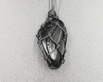 May include: Black gemstone pendant with a black cord necklace. The gemstone is wrapped in a black macrame knot.
