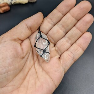 May include: A clear quartz crystal pendant wrapped in black cord. The crystal is faceted and has a natural, raw shape.