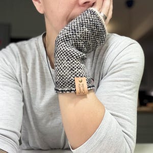 May include: Black and white knitted fingerless gloves with a brown leather tag that says "Sancta Cecilia".