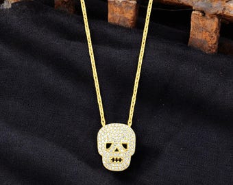 Puede incluir: Un collar de cadena dorada con un pequeño colgante de calavera pavé. La calavera está hecha de piedras de circonita cúbica transparentes.