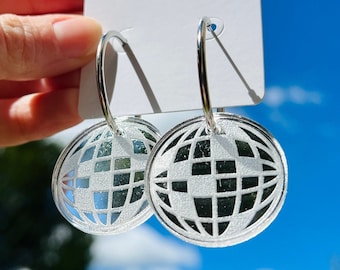 May include: Silver hoop earrings with a white globe design. The earrings are on a white card with the text "Nomad Kandi" in pink and purple.