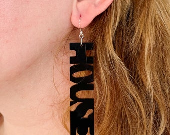 May include: Black acrylic earrings with the word "HOUSE" spelled vertically.