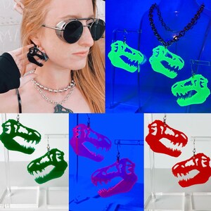 May include: A set of three pairs of dinosaur skull earrings. The earrings are made of acrylic and glow in the dark. The earrings are available in green, red, and pink.