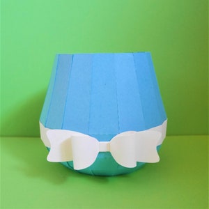 Könnte beinhalten: Eine hellblaue Papier-Vase mit einer weißen Papier-Schleife. Die Vase ist aus gefaltetem Papier und hat ein geriffeltes Design.