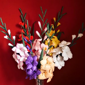 May include: A bouquet of paper flowers in a variety of colors, including red, pink, white, purple, and yellow. The flowers are arranged in a vase and are set against a red background.