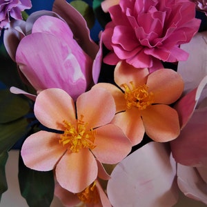 May include: A bouquet of pink and peach paper flowers with green leaves. The flowers are arranged in a vase.