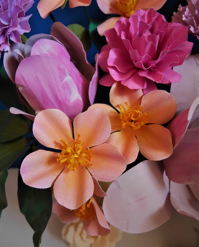 May include: A bouquet of pink and peach paper flowers with green leaves. The flowers are arranged in a vase.