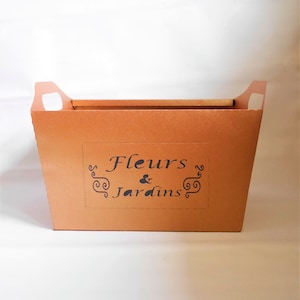 Könnte beinhalten: Ein brauner Karton mit einem Griff an jeder Seite. Der Karton hat ein Etikett mit der Aufschrift "Fleurs & Jardins" in schwarzen Buchstaben.