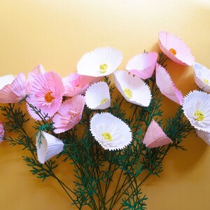 Puede incluir: Un ramo de flores de papel rosa y blanco con tallos verdes. Las flores están dispuestas en forma de abanico y tienen una textura delicada y rizada.