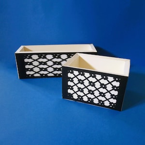 Può includere: Due scatole bianche con motivi geometrici neri. Le scatole sono in cartone e hanno un design decorativo.