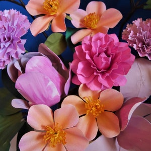 May include: A bouquet of paper flowers in shades of pink, peach, and white. The flowers are arranged in a vase and include carnations, roses, and lilies.