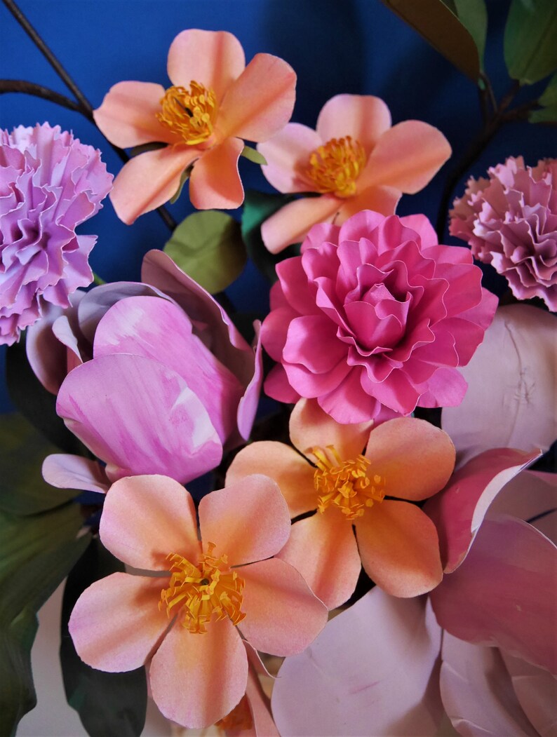 May include: A bouquet of paper flowers in shades of pink, peach, and white. The flowers are arranged in a vase and include carnations, roses, and lilies.