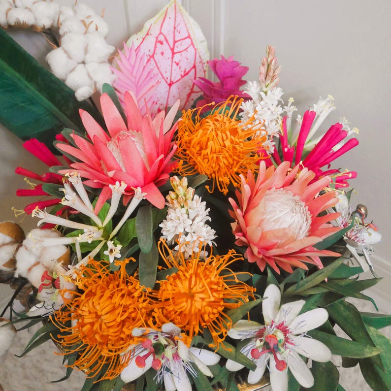 May include: A vibrant bouquet of tropical flowers, including orange, pink, and white blooms, arranged in a lush green foliage setting.