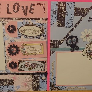 May include: Two scrapbook pages with a pink and blue background. The left page has the text "TRUE LOVE" and the right page has the text "BLOOM". Both pages feature floral designs and blank spaces for photographs.