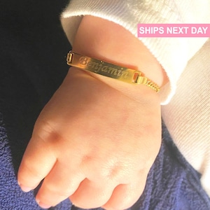 May include: Gold baby bracelet with a personalized nameplate engraved with the name "Benjamin".