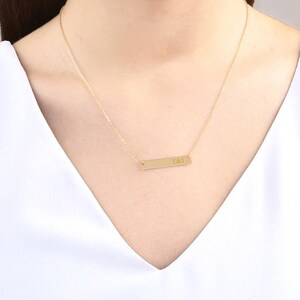 May include: A gold chain necklace with a thin, rectangular bar pendant engraved with the initials "T&J".