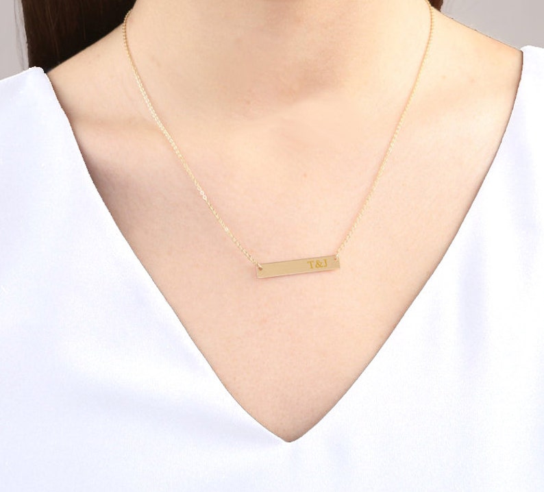 May include: A gold chain necklace with a thin, rectangular bar pendant engraved with the initials "T&J".