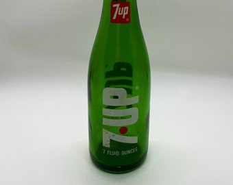 May include: A green glass 7 Up bottle with a red and white 7 Up logo. The bottle is 7 fluid ounces.