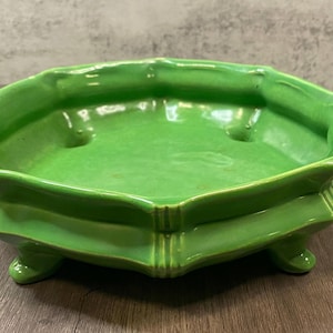 Peut inclure: Un pot de fleurs en céramique vert vif avec un bord festonné et trois petits pieds. Le pot a une finition brillante et une conception peu profonde et ouverte, adaptée aux petites plantes ou à un usage décoratif.